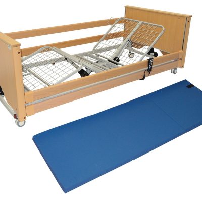 A picture of a crash mat, which has been unfolded and is on the floor alongside a bed frame.